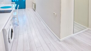 Een moderne, goed verlichte kamer met een blauwe deur, een witte wasmachine en een grote spiegel.