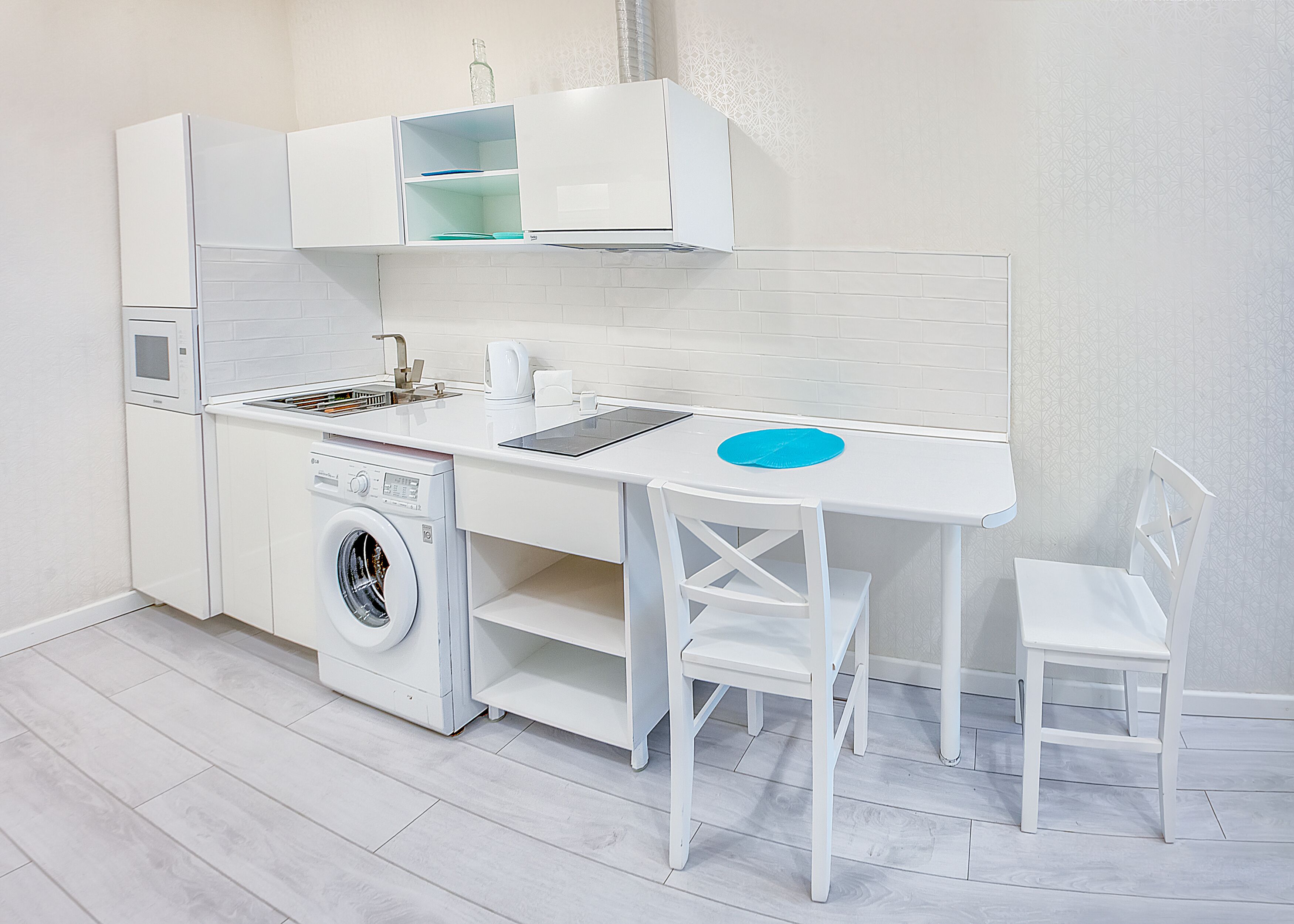 A compact kitchenette with a washing machine, a sink, and a small table with chairs.