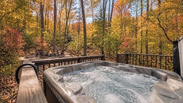 Een hottub omgeven door een houten terras, met uitzicht op een bebost gebied.
