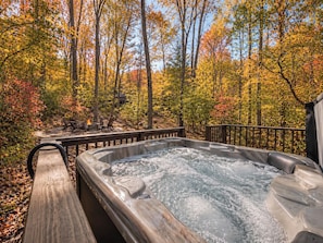 A hot tub surrounded by a wooden deck, with a view of a forested area.