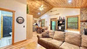 Una sala de estar acogedora con techo de madera, un sofá de cuero marrón, una zona de comedor con mobiliario de madera y una chimenea de piedra.
