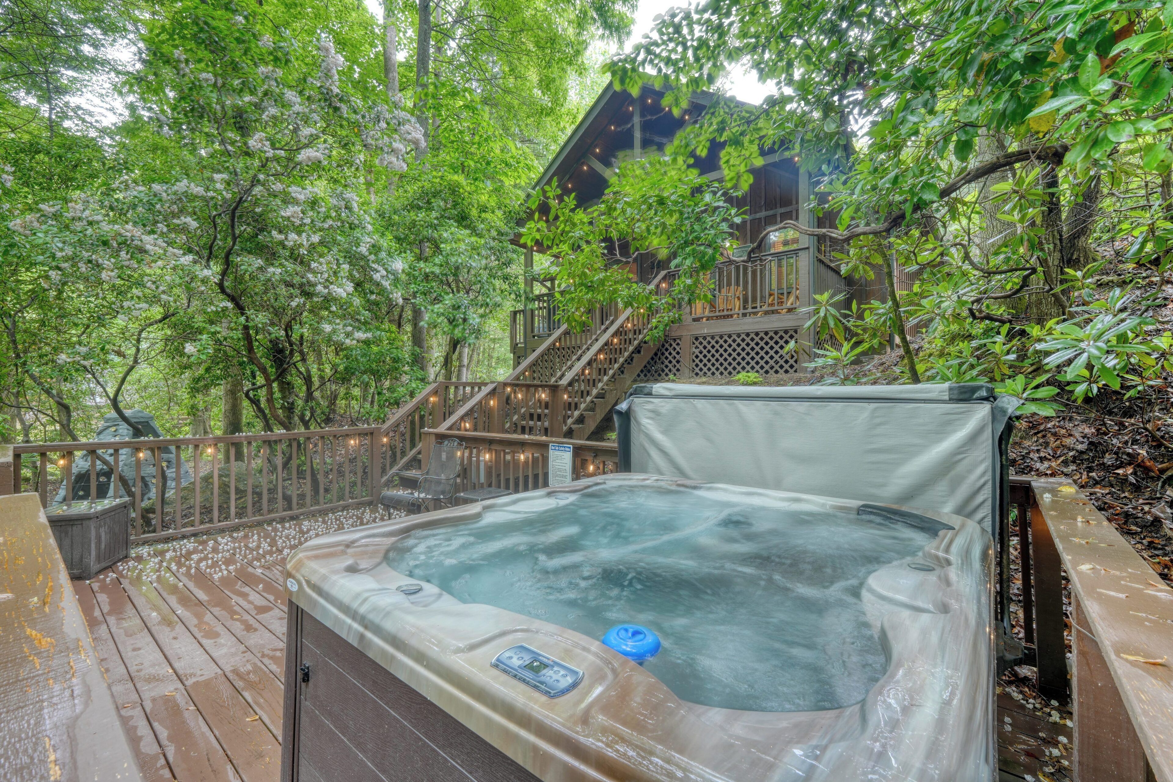 Un bain à remous sur une terrasse en bois, entouré d’arbres, avec un escalier en bois menant à un bâtiment.