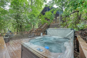 Un jacuzzi en una terraza de madera rodeado de árboles, con una escalera de madera que lleva a un edificio.