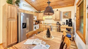 Una cocina con armarios de madera, un refrigerador de acero inoxidable, una lámpara colgante y una mesa de comedor con sillas.