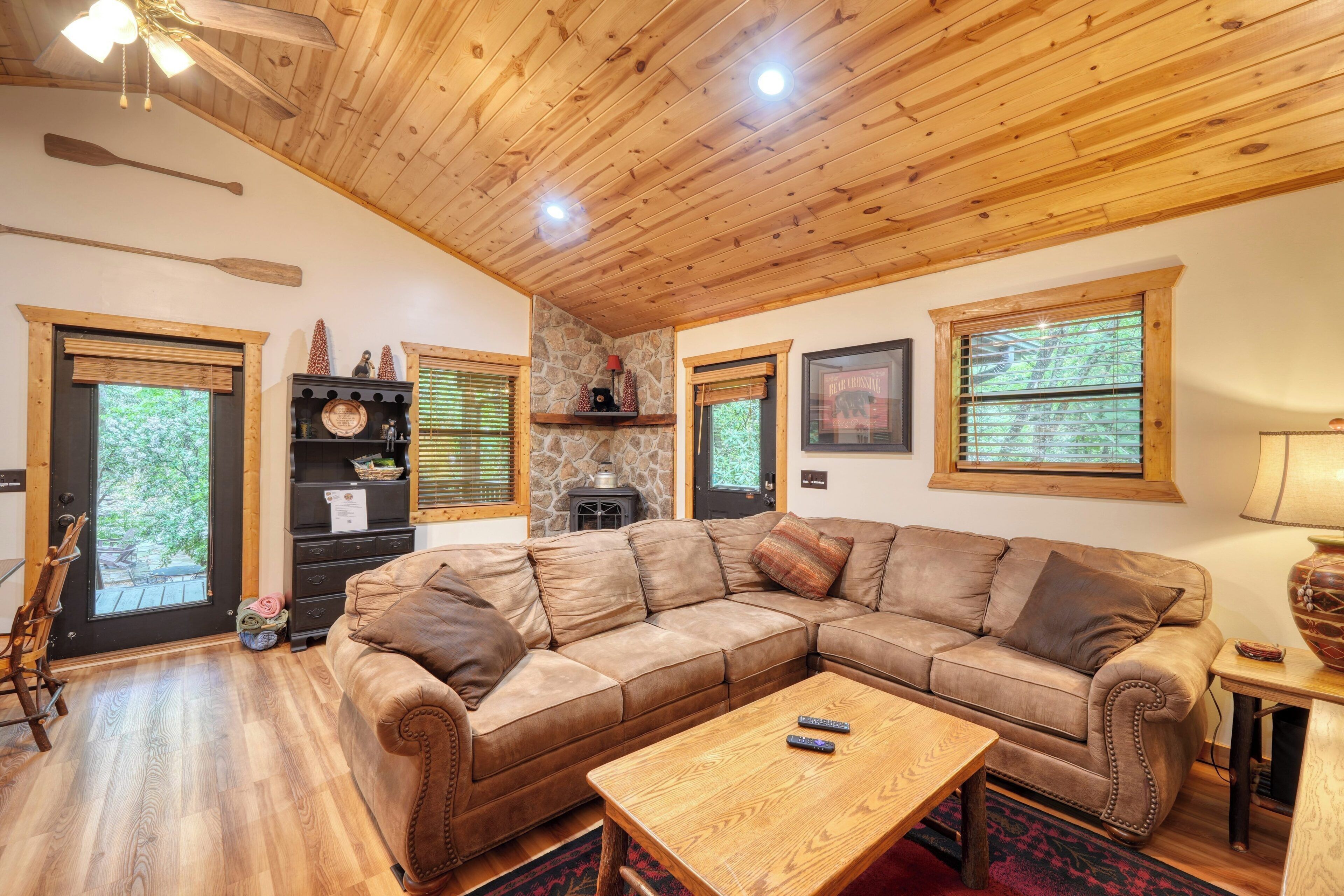 A cozy living room with a wooden ceiling, a large sectional sofa, a coffee table, and a stone fireplace.