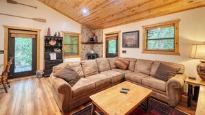 Una sala de estar acogedora con techo de madera, un amplio sofá modular, una mesa de centro y una chimenea de piedra.