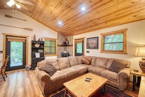 Ein gemütliches Wohnzimmer mit Holzboden, einem großzügigen Ecksofa, einem Couchtisch und einem Kamin aus Stein.