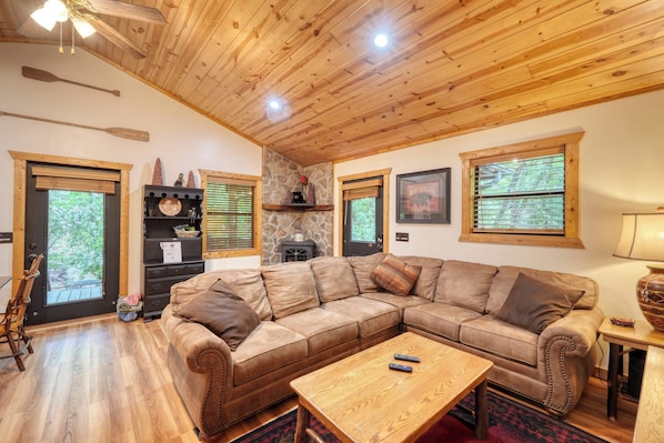 A cozy living room with a wooden ceiling, a large sectional sofa, a coffee table, and a stone fireplace.