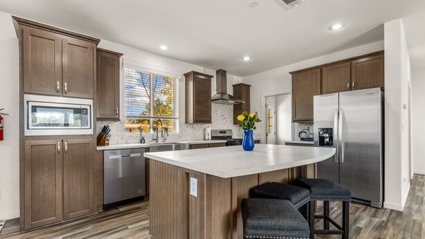 A modern kitchen with wooden cabinets, a large island with bar stools, stainless steel appliances, and a window with a view of trees. - Andante Trail - Unit A - Red Rock Retreat (Sedona)