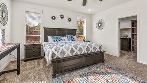 A bedroom with a dark wood bed, a ceiling fan, and a large window with blinds. - Andante Trail - Unit A - Red Rock Retreat (Sedona)