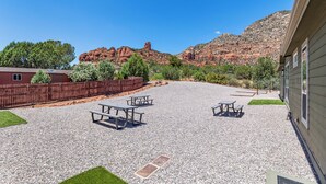 A gravel patio with picnic tables, a wooden fence, and a building with windows. - Andante Trail - Unit A - Red Rock Retreat (Sedona)