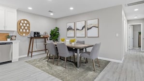 A modern kitchen with white cabinets, a wooden table, and a gray rug. - Wine Lovers Paradise (Lodi)