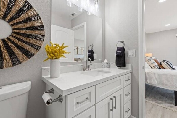A modern bathroom with a white sink, mirror, and toilet. There is a decorative wall piece above the sink and a towel rack with a towel hanging on it.