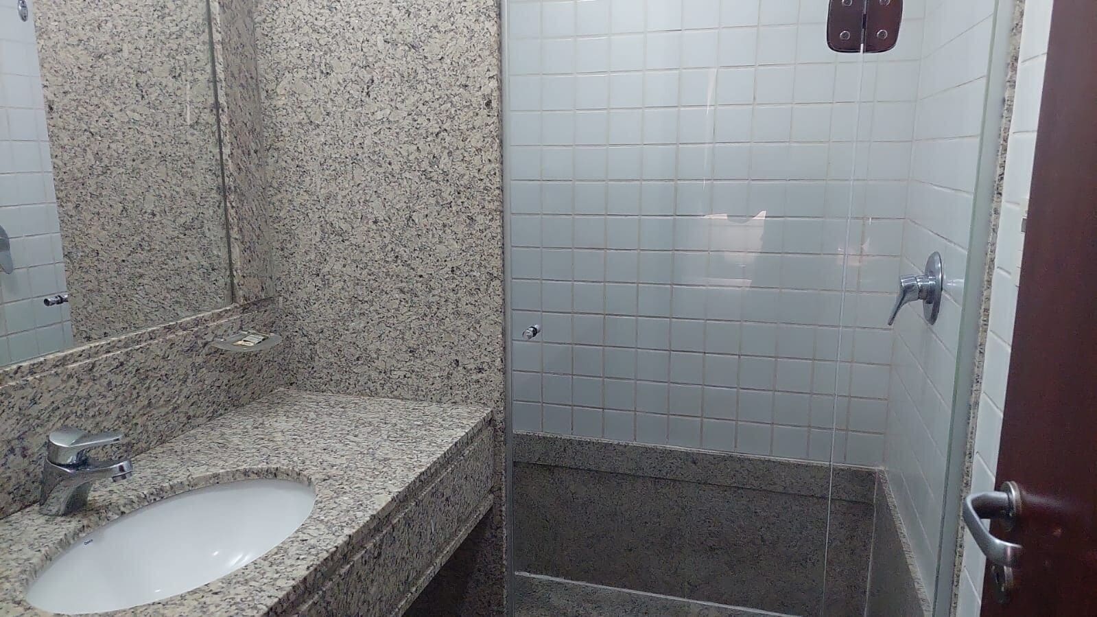 A bathroom with a granite countertop sink, a mirror, and a shower area with white tiles.