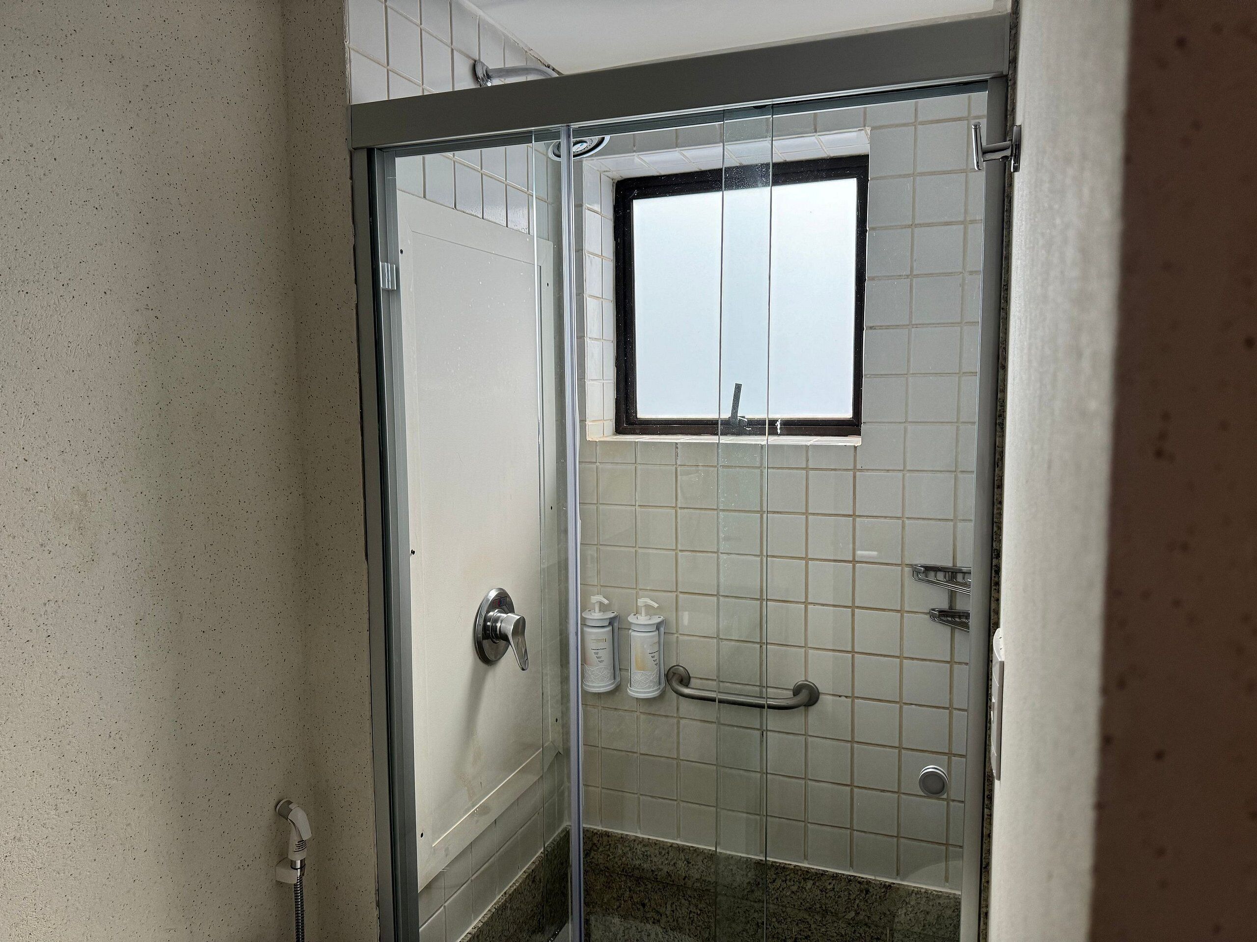 A glass-enclosed shower with a window, tiled walls, and a grab bar.