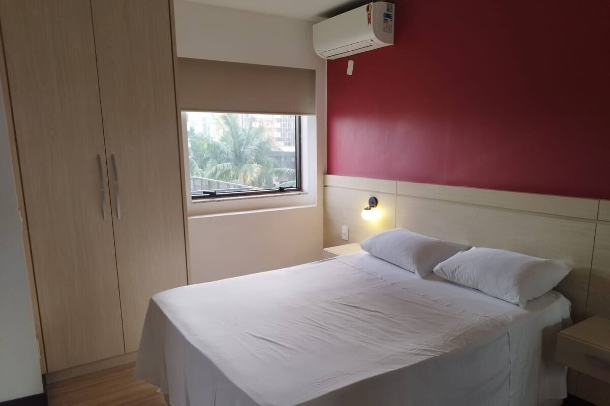 A bedroom with a bed, a window, a wardrobe, and an air conditioning unit.