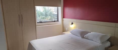 A bedroom with a bed, a window, a wardrobe, and an air conditioning unit.