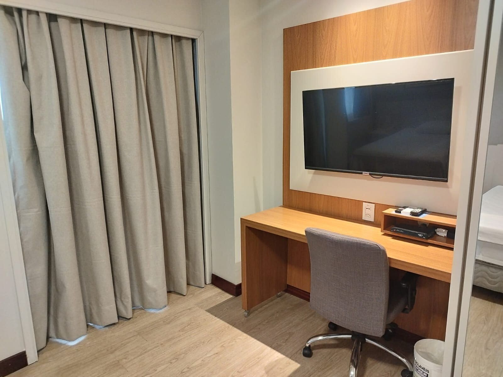 Una habitación de hotel con un escritorio de madera, un televisor de pantalla plana y una silla de oficina gris.