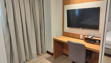 Una habitación de hotel con un escritorio de madera, un televisor de pantalla plana y una silla de oficina gris.