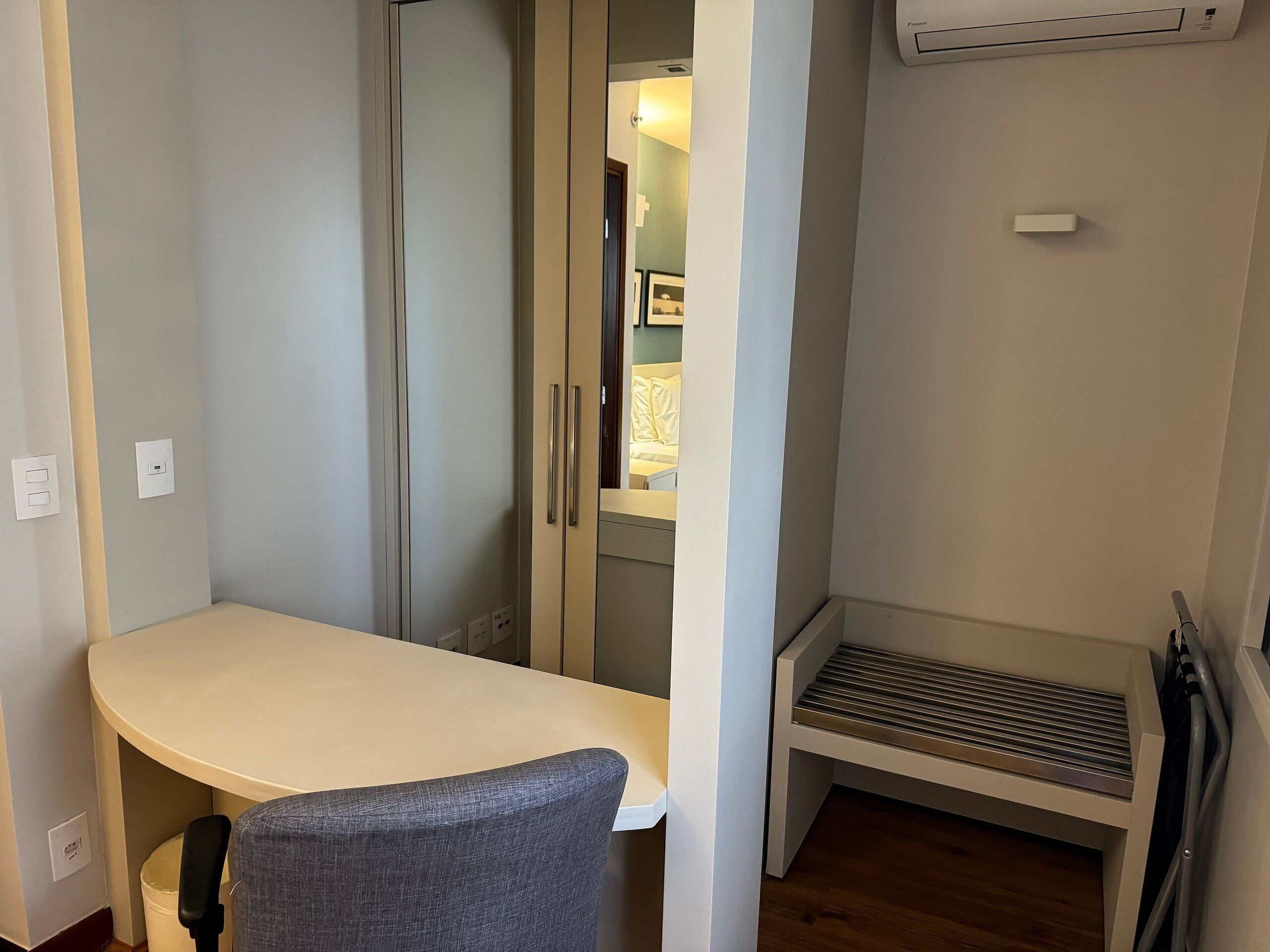 A compact room with a small table and a chair, a sliding door leading to another room, a vent, and a power outlet.
