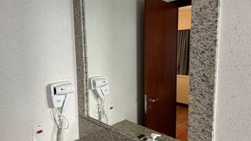 A bathroom with a granite countertop, a mirror, a hairdryer, and a towel dispenser.