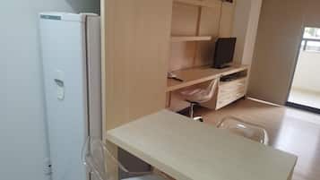 Una habitación compacta con un escritorio de madera, una silla, un televisor pequeño y un refrigerador.
