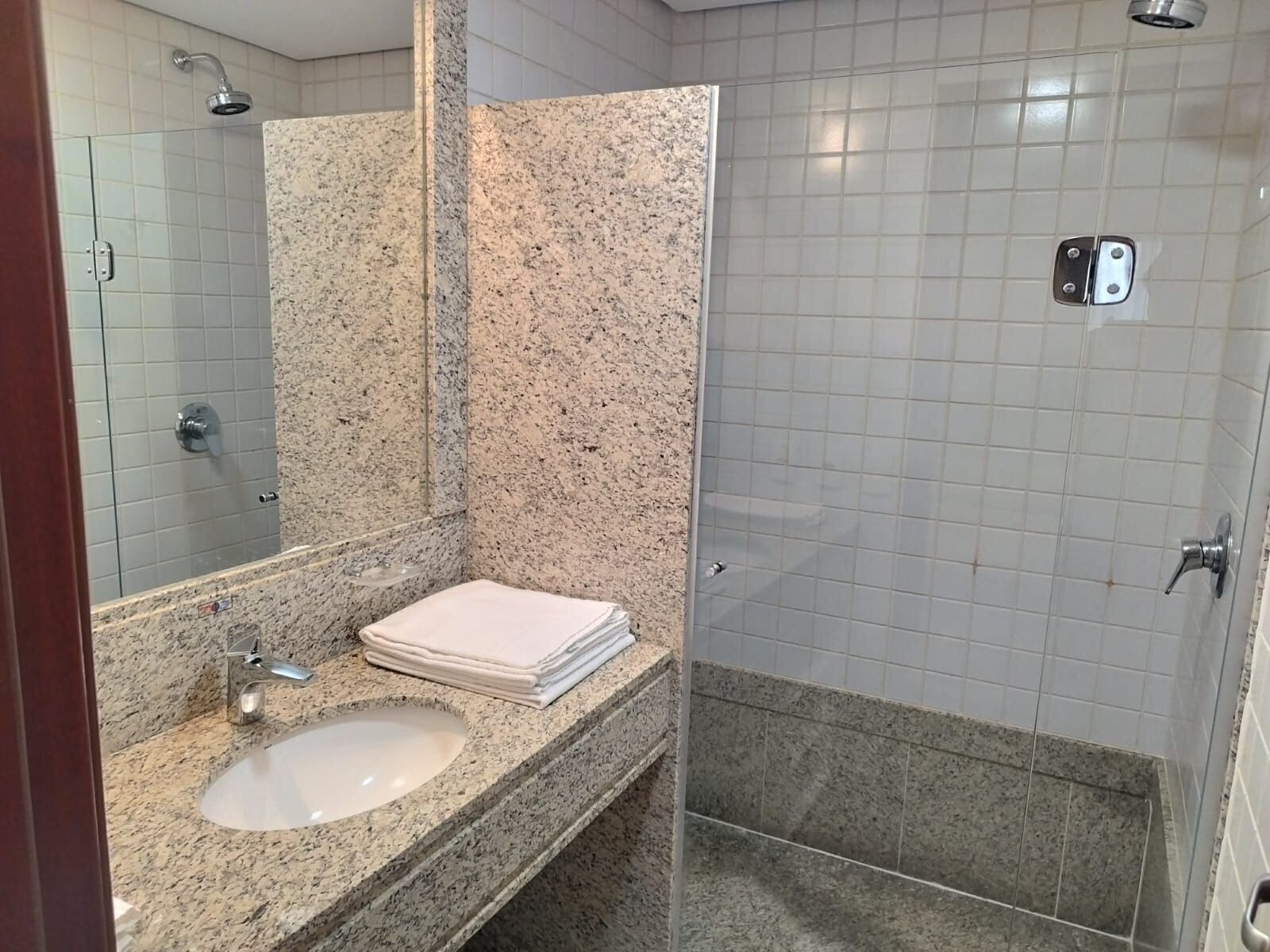 A bathroom with a granite countertop sink, a mirror, and a shower area with a glass door.