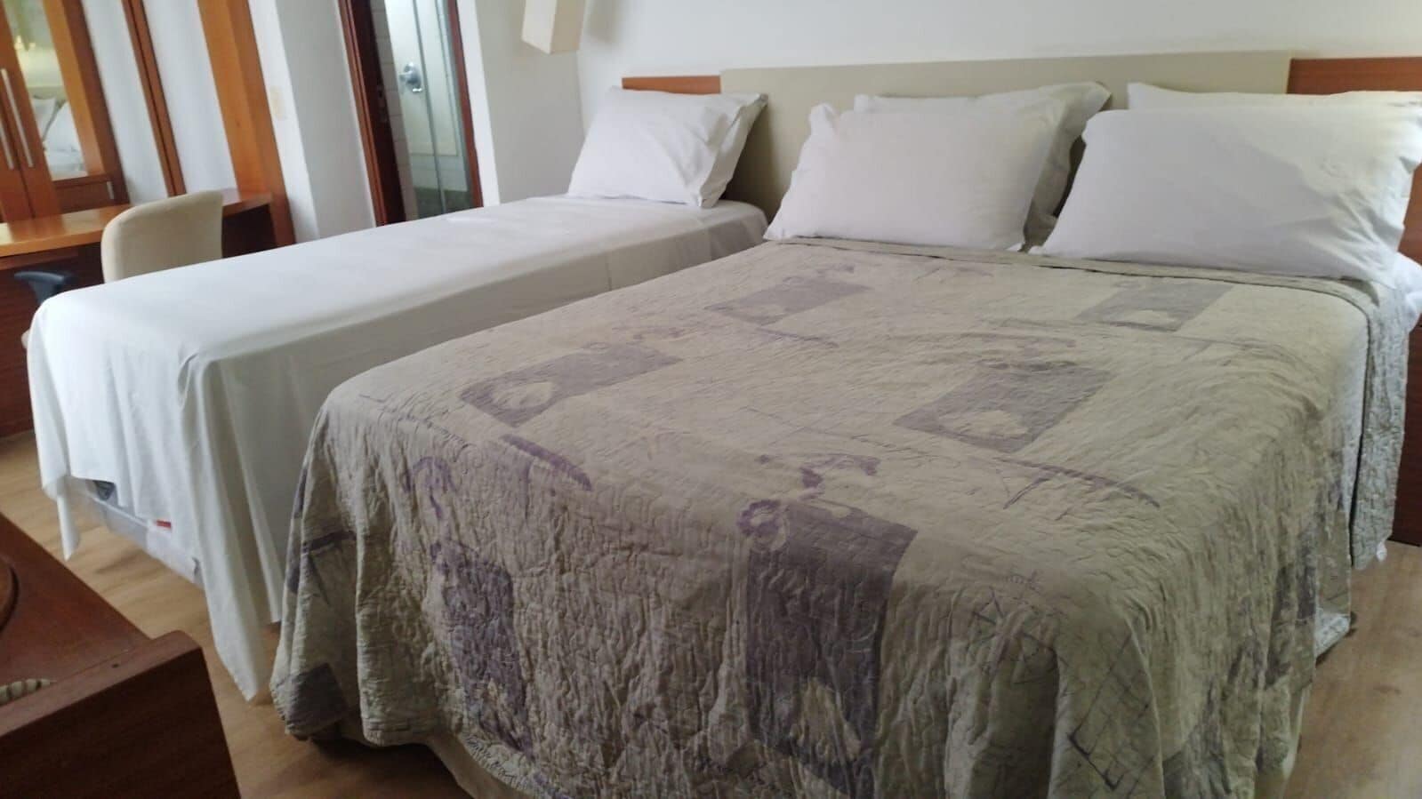 A hotel room with two beds, a wooden desk, and a chair.