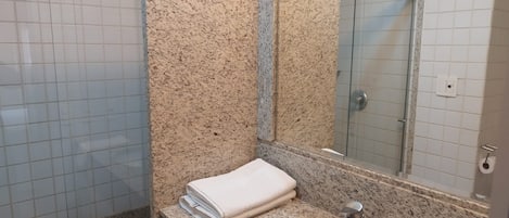 A bathroom with a granite countertop, a sink, a mirror, and a shower.