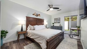 A bedroom with a wooden bed, bedside lamps, a ceiling fan, a dresser, and a view of the outdoors. - Peaceful APT by Lakebottom w Arcade/8mi FT Benning (Columbus)