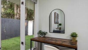 A room with a wooden desk, a white chair, a large mirror, and a view of a backyard with a fence and greenery. - Peaceful APT by Lakebottom w Arcade/8mi FT Benning (Columbus)