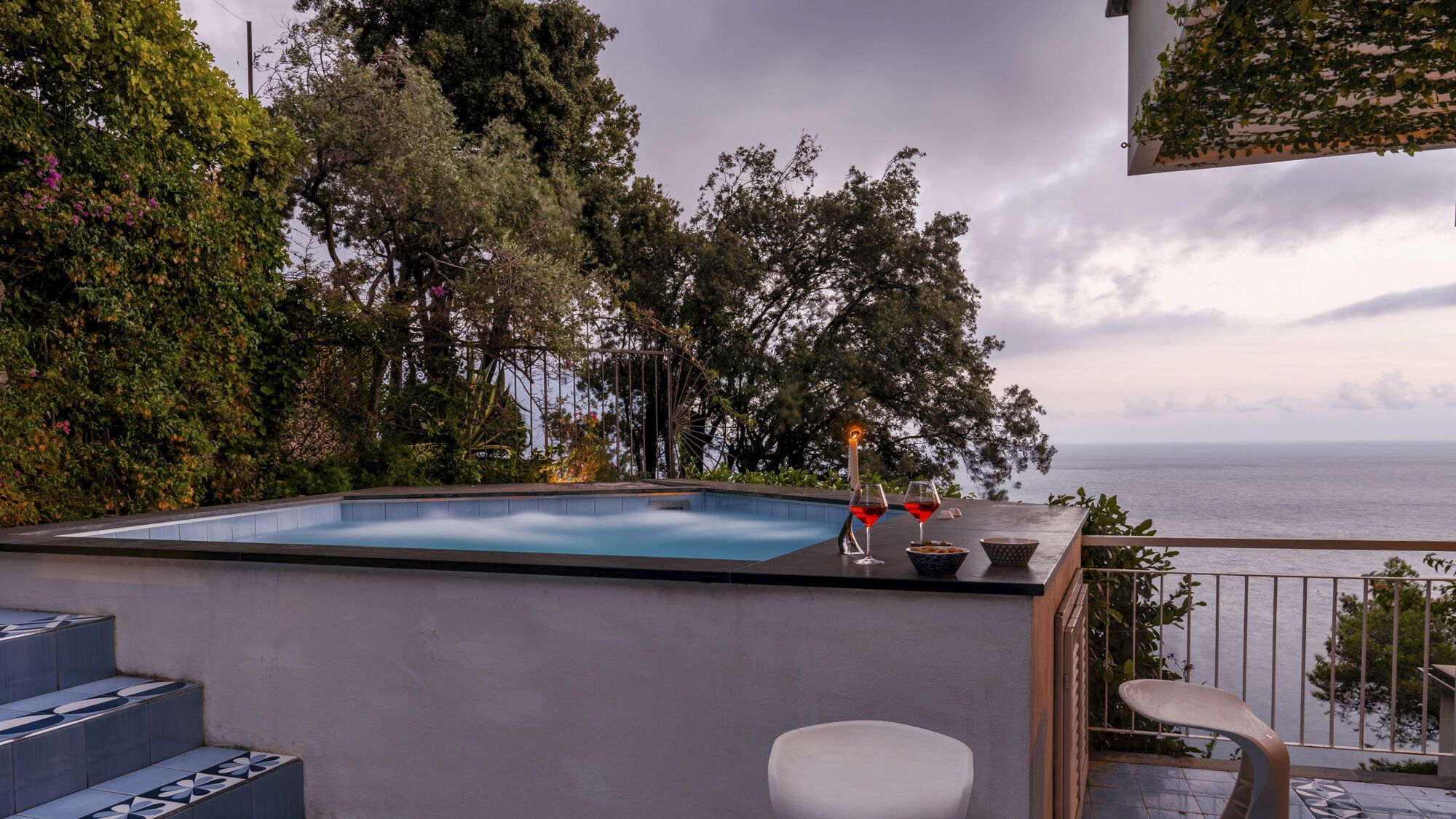 Una piscina en la azotea con vista al mar, rodeada de exuberante vegetación y una noria.