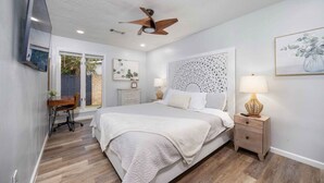 Un dormitorio con cama, mesita de noche, lámpara y una obra de arte.