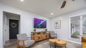 Una sala de estar moderna con un mueble aparador de madera en espiga, dos sillones grises, una mesa de centro redonda de madera y un televisor de pantalla plana grande montado en la pared.