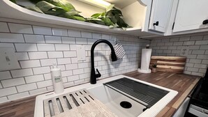 A kitchen with a white tiled backsplash, a wooden countertop, a sink with a black faucet, and a dish rack.