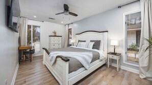 A bedroom with a bed, bedside tables, a desk, a chair, a ceiling fan, and a window with blinds.