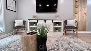 A living room with a flat-screen TV, two chairs, a coffee table, a sideboard, and a patterned rug.