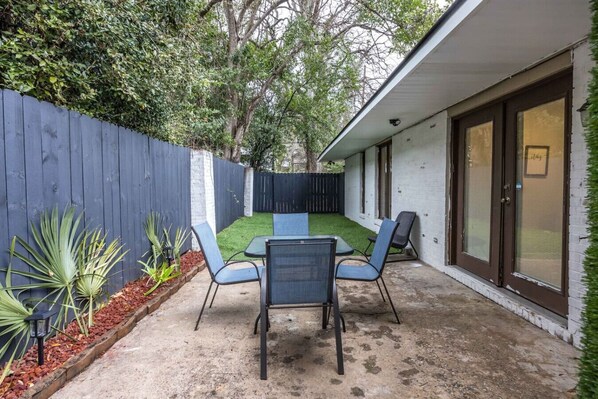 A patio with a table and chairs, a blue fence, and a white building with a garage door.