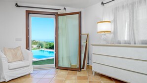 Una habitación con sofá blanco, vista a una piscina, puerta corredera de vidrio y una lámpara sobre una cómoda.