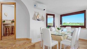 Un comedor con mesa de vidrio, sillas blancas y vistas al exterior.