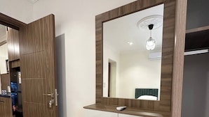 A hotel room with a wooden wardrobe, a vanity with a mirror, a bench, and patterned floor tiles. - 3 Antica Jabalal-lwebdeh (Amman)