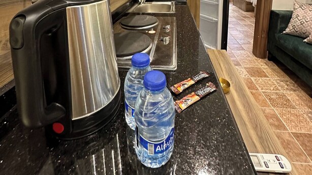 A kitchen with a kettle, water bottles, a scale, and a remote control on the counter. - 3 Antica Jabalal-lwebdeh (Amman)