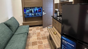 A compact living space with a sofa, a TV mounted on a wooden panel, a refrigerator, and a microwave. - 3 Antica Jabalal-lwebdeh (Amman)