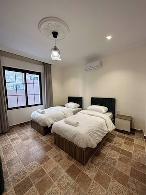 Une chambre d’hôtel avec deux lits, une fenêtre avec des rideaux, un luminaire au plafond et un appareil de climatisation.