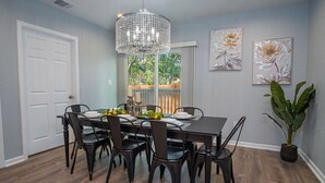 A dining room with a dark wooden table set for six, surrounded by black chairs. A large crystal chandelier hangs above. - Escape to 4BR/3BA Brand New Downtown Home (San Antonio)