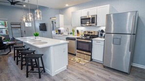 A modern kitchen with white cabinets, stainless steel appliances, and a central island with stools. - Escape to 4BR/3BA Brand New Downtown Home (San Antonio)