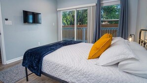 A bedroom with a bed, a television mounted on the wall, and a sliding glass door leading to an outdoor area. - Escape to 4BR/3BA Brand New Downtown Home (San Antonio)