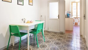 Ein Essbereich mit einem weißen Tisch und zwei grünen Stühlen, einer weißen Tür, gemusterten Bodenfliesen und gerahmten Bildern an der Wand.