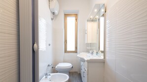 Ein schmales Badezimmer mit Toilette, Bidet und Waschbecken.