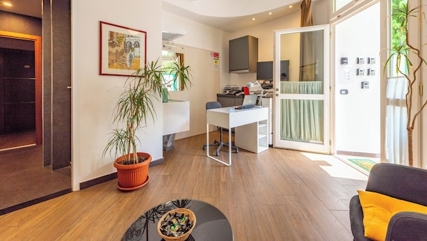 A modern hotel lobby with a reception desk, a seating area with a coffee table, a potted plant, and a large window offering a view of the outdoors. - Andenis Tiber House  (Rome)